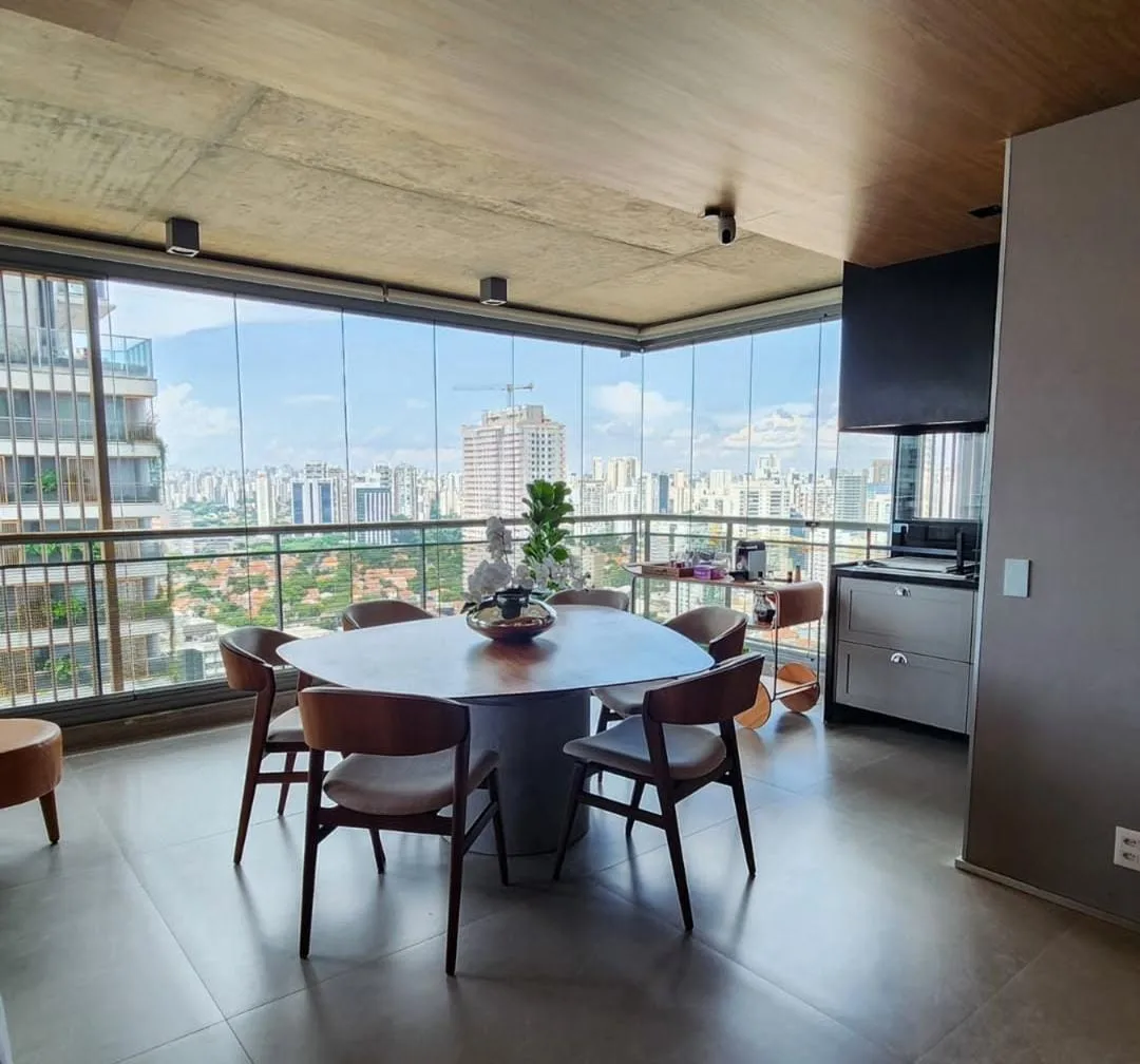 Varanda gourmet envidraçada com mesa de jantar e cozinha ao fundo