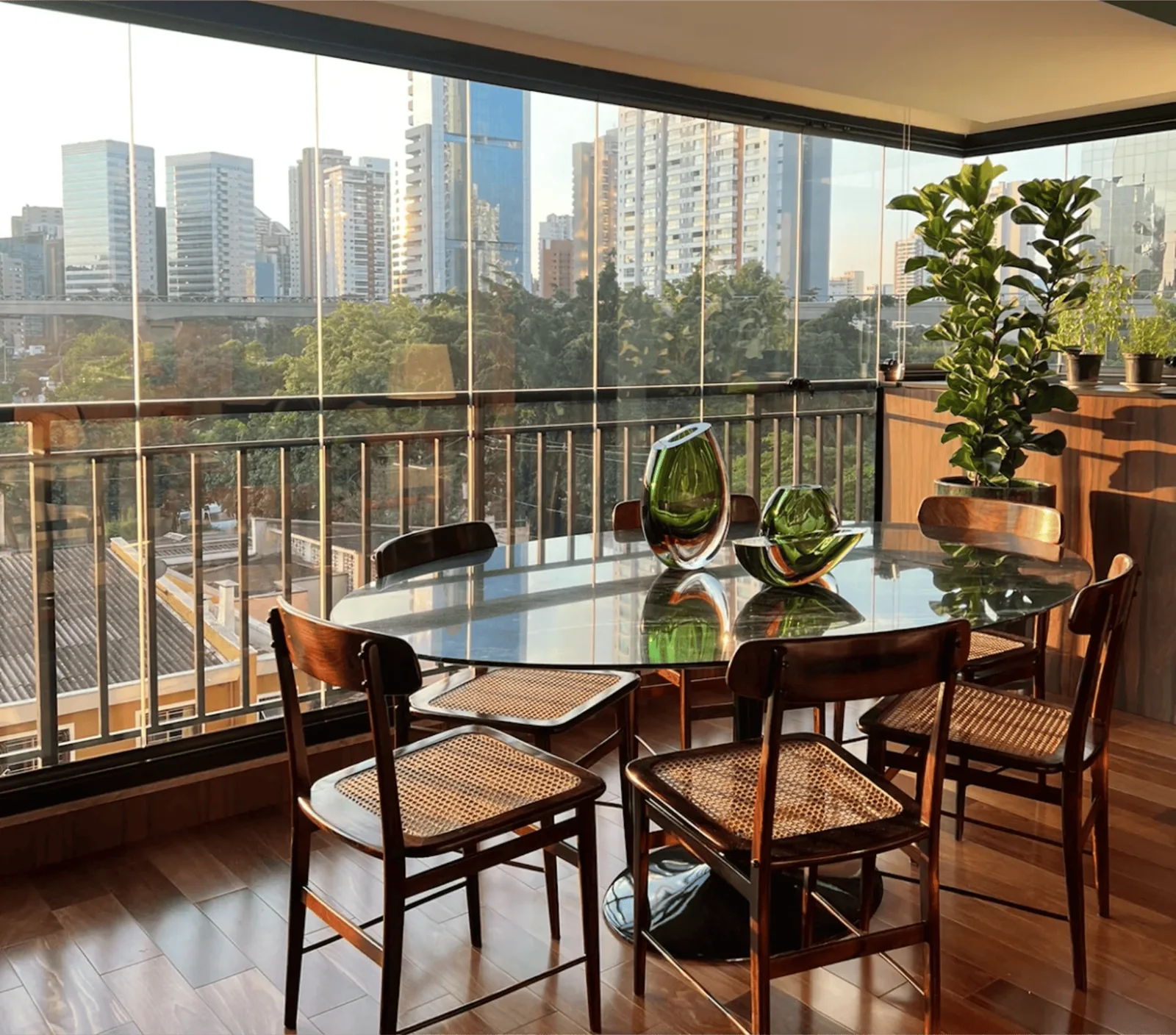 Varanda envidraçada com mesa de jantar e vista para a cidade ao entardecer