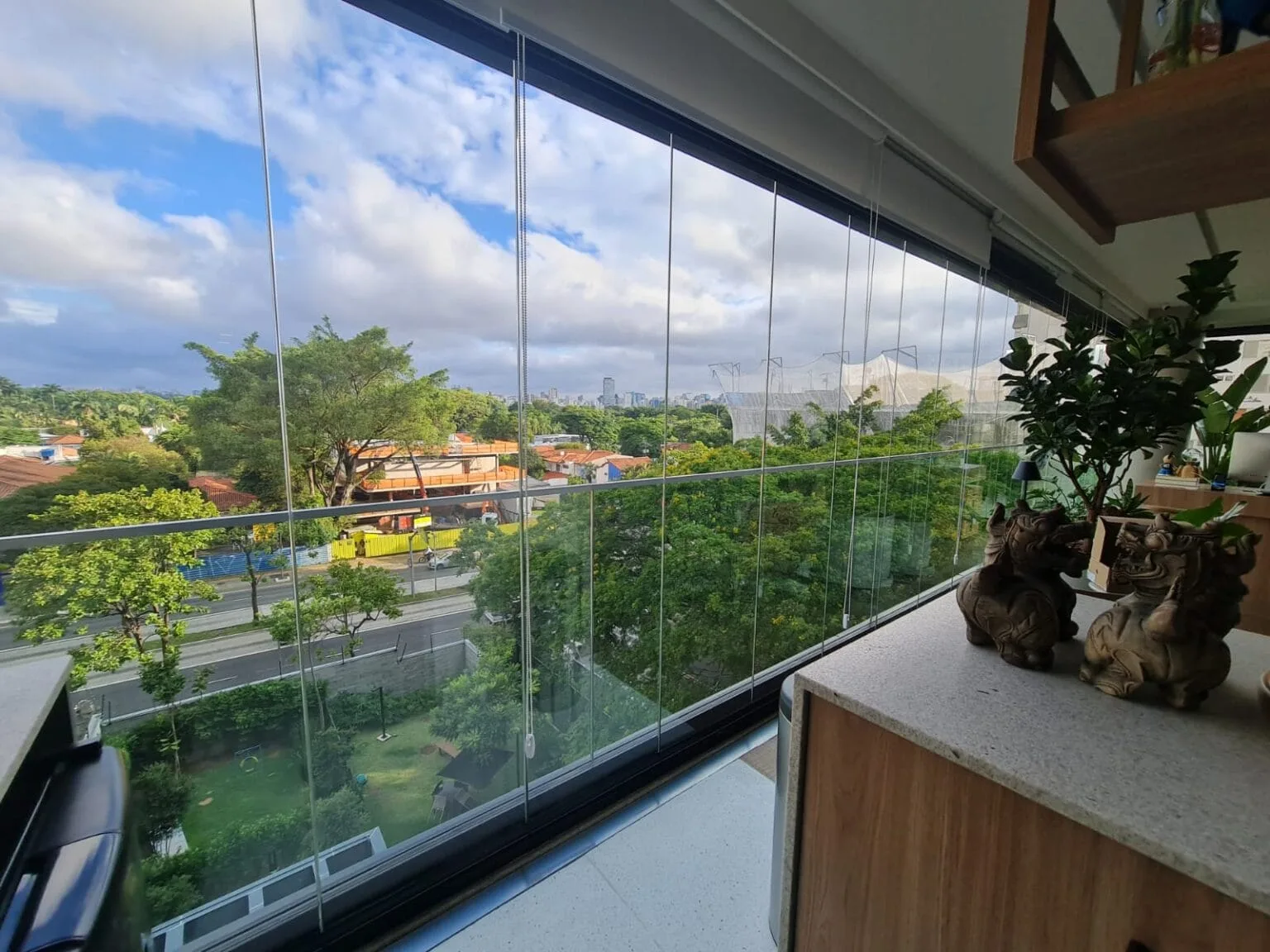 Sacada envidraçada com vista para área verde e avenida arborizada